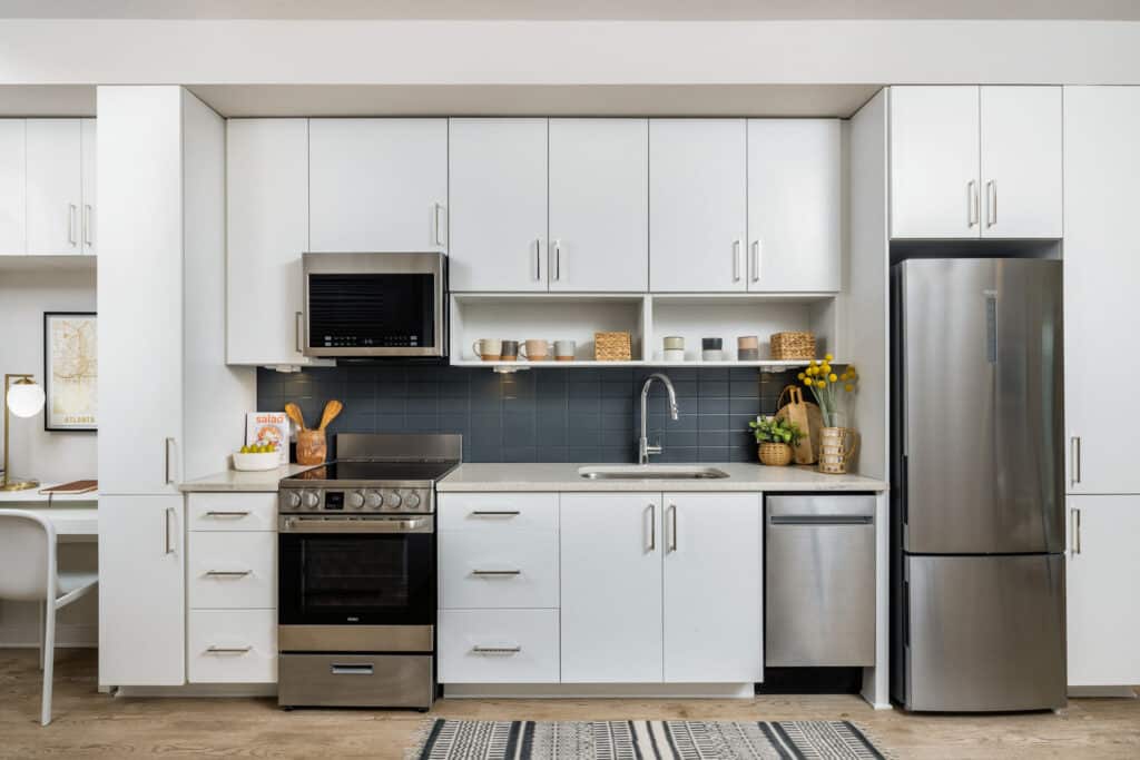 Modern kitchen with white cabinets, stainless steel appliances, a blue tile backsplash, and wooden countertop accents. A small collection of kitchenware sits on open shelves and the countertop.