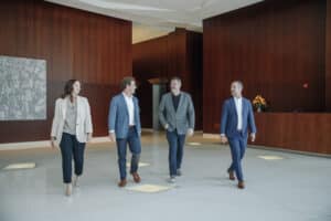 Four people in business attire walk through a modern office lobby with dark wood walls and a reception desk.